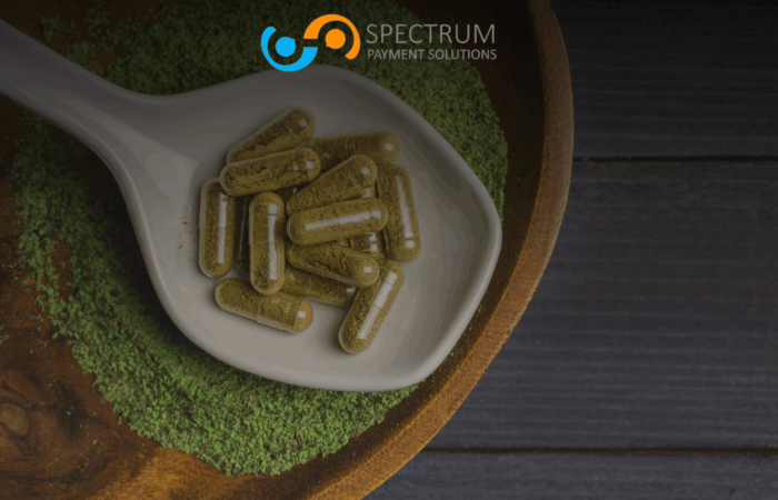 Kratom capsules on white spoon with green kratom powder - Spectrum Payment Solutions merchant processing
